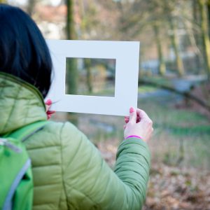 Waldbaden: Frau schaut durch Bilderrahmen in den Wald